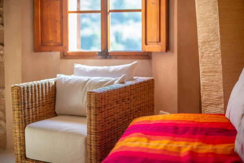 A bedroom with a woven armchair beside a bed and an open window.