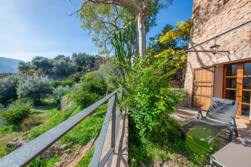 A patio beside a stone building overlooks a lush garden and distant hills.
