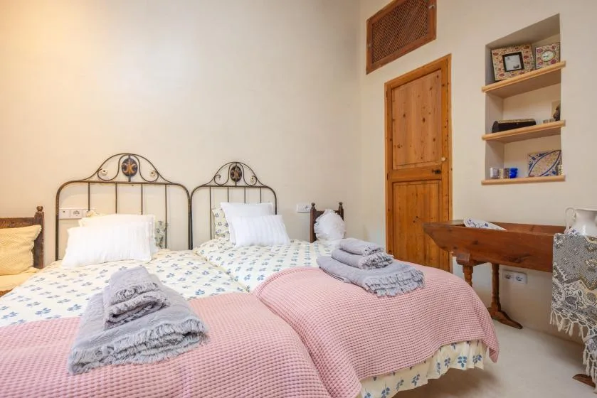 A bedroom with two beds covered in patterned bedding and pink blankets.