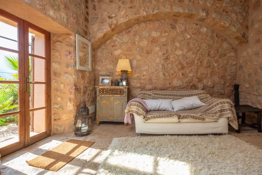A stone-walled bedroom with a bed, bedside cabinet, and open wooden doors.