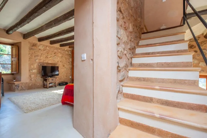 A rustic living room opens onto a staircase, with exposed beams and stone walls.