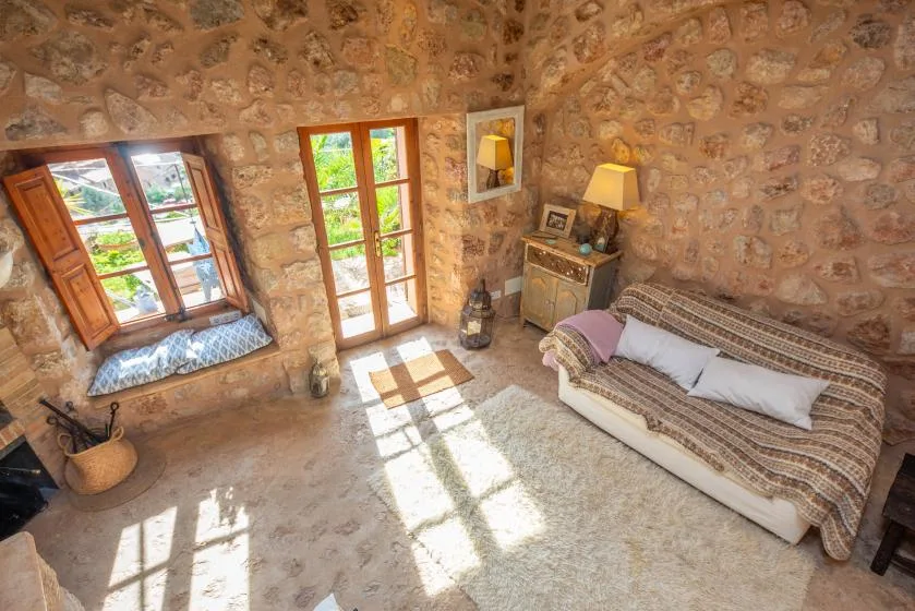A stone-walled bedroom with a bed, wooden windows, and a glass door.