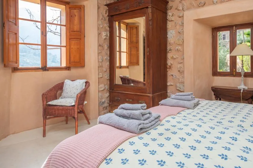 A bedroom with a bed, a wooden wardrobe, and a chair beside the window.