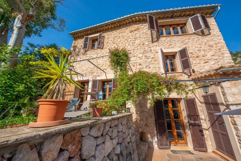 A stone house exterior with wooden shutters and a leafy terrace.