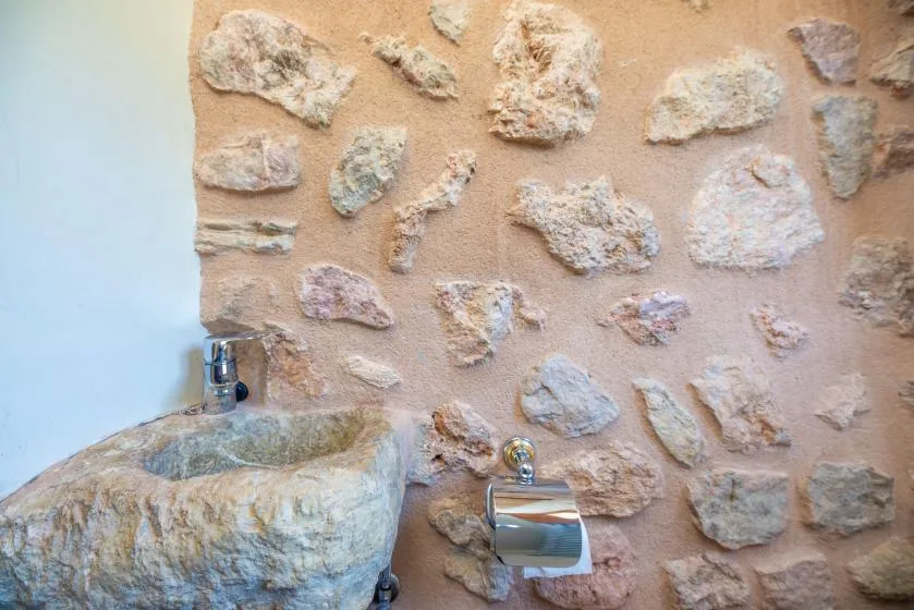 A stone sink and faucet stand against a textured stone wall.