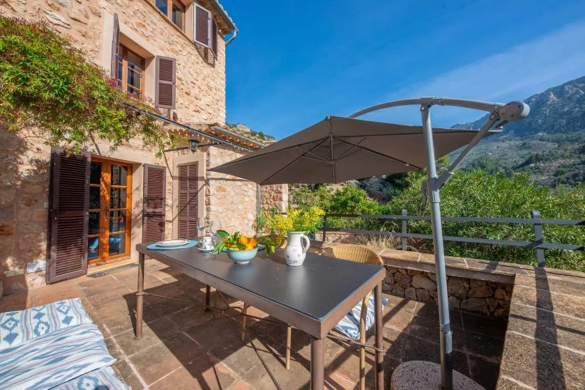 A stone terrace has an outdoor dining table beneath a large umbrella.