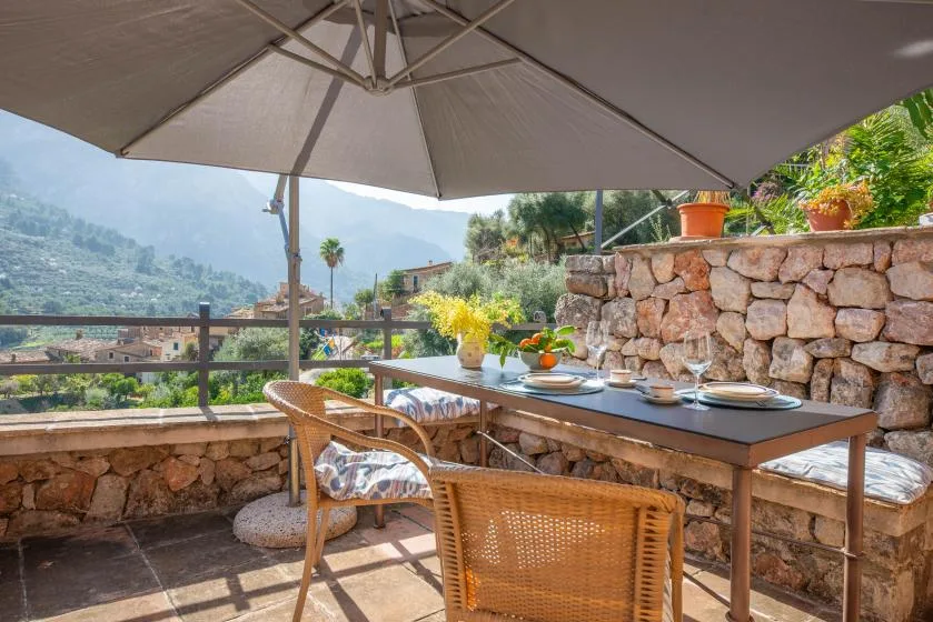 An outdoor dining terrace with a table and wicker seating overlooks a green hillside.