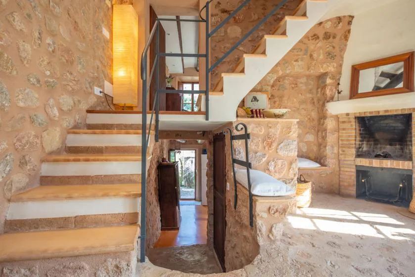 A rustic stone living area with a staircase and fireplace.