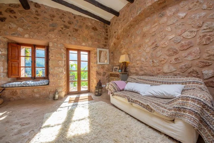 A stone-walled room with a cushioned seating area and sunlight through the windows.
