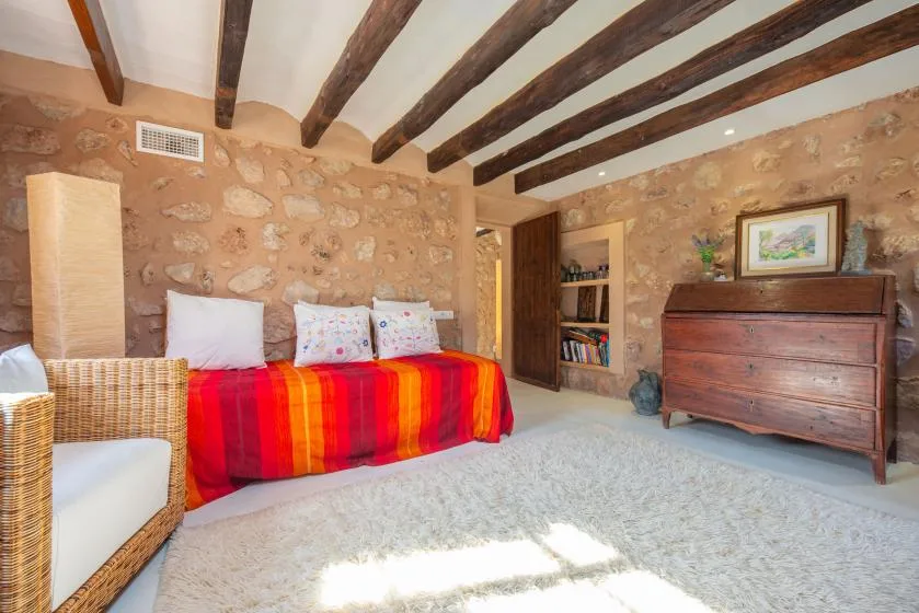 A rustic bedroom with a colorful bedspread, exposed ceiling beams, and stone walls.