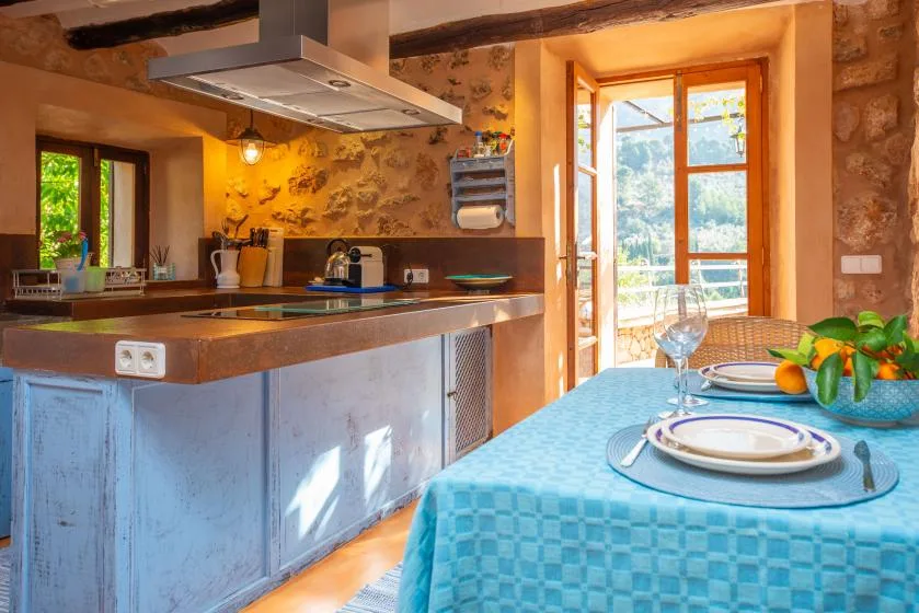 A rustic kitchen and dining area with a turquoise tablecloth and large windows.