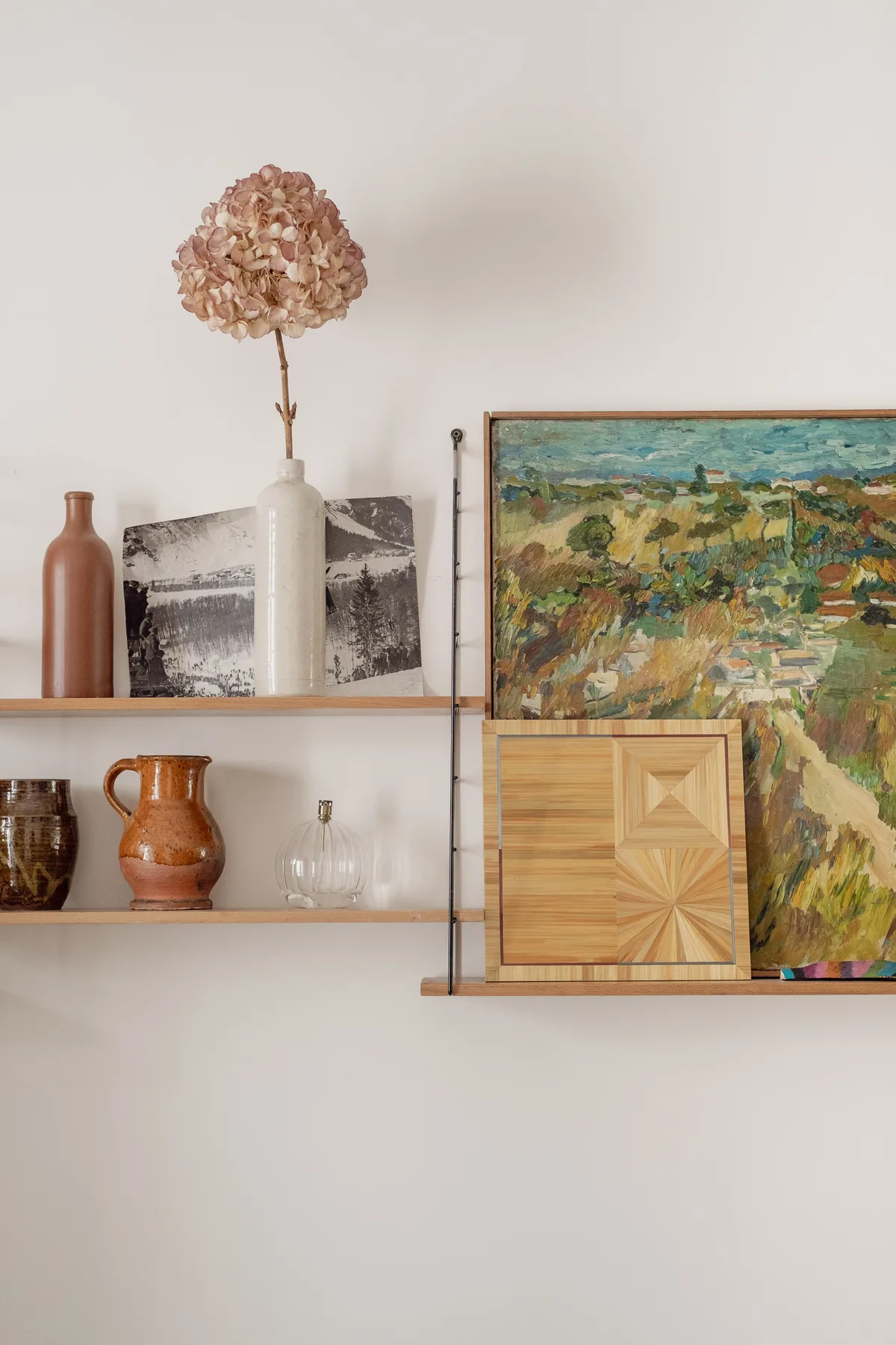 A wall display features framed artwork, decorative pottery, and dried flowers on shelves.