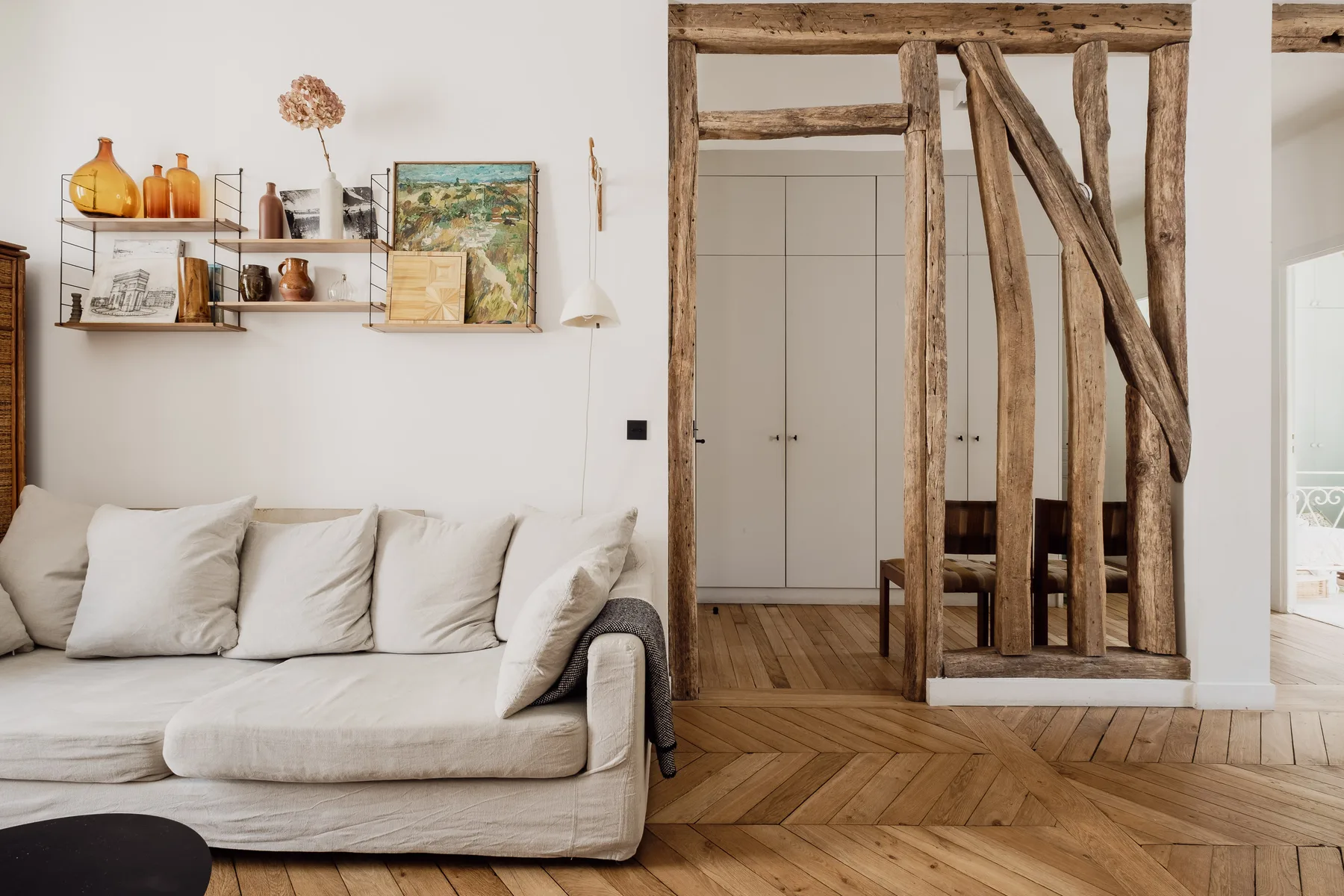 A bright living room with a light-colored sofa and shelves displaying pottery and artwork.