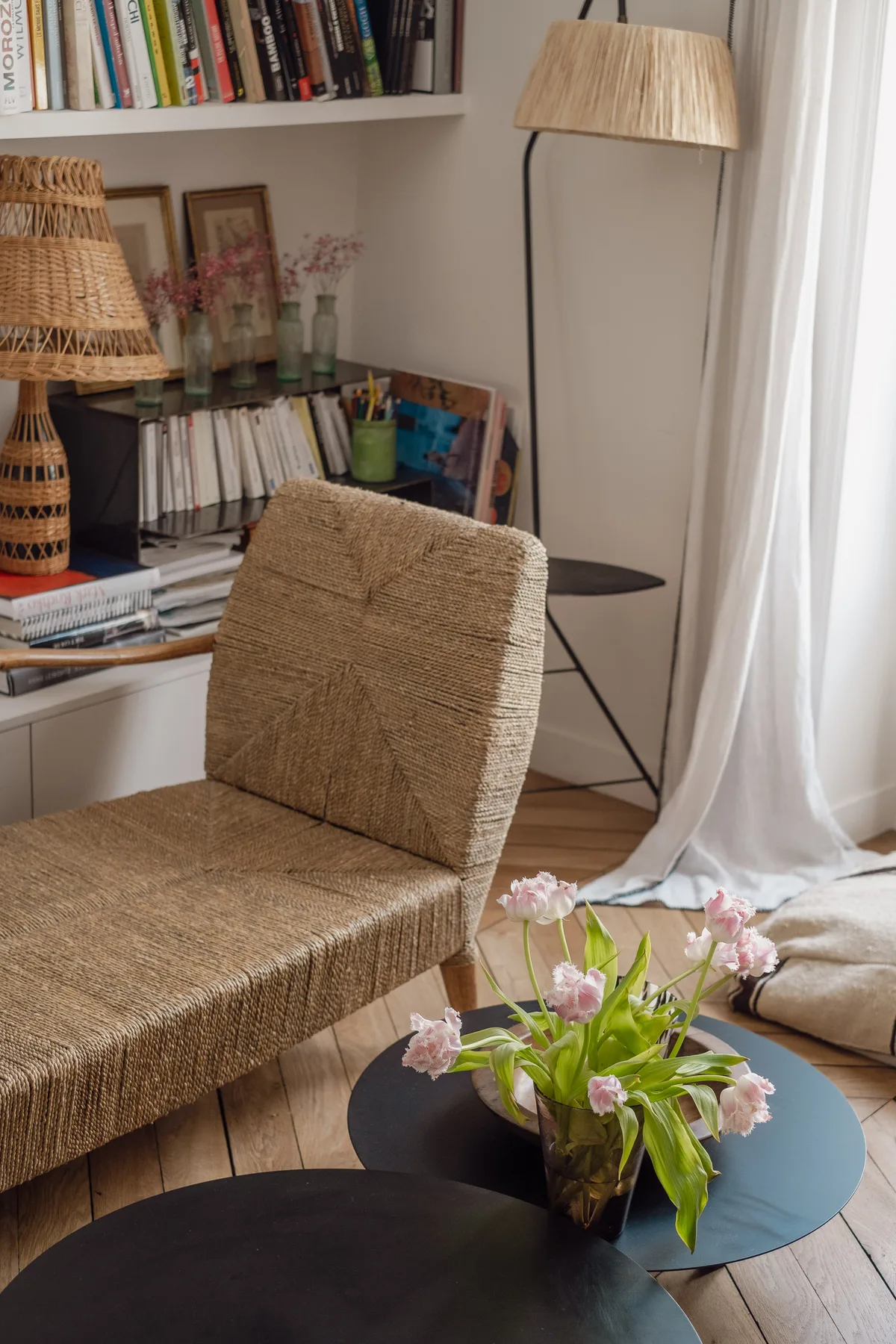 A cozy reading area with woven seating, bookshelves, and flowers on a round table.