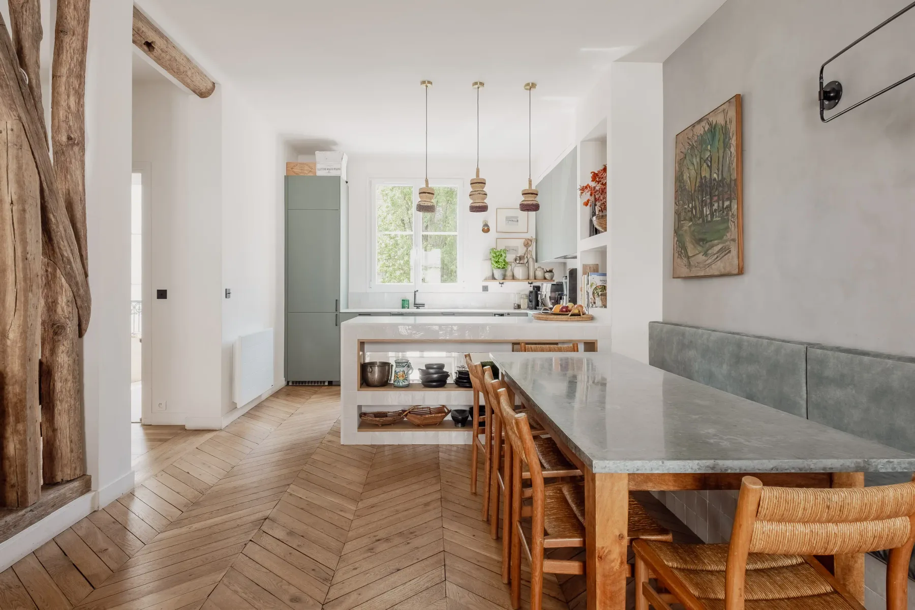 A bright kitchen with a long island, wooden seating, and pendant lights.