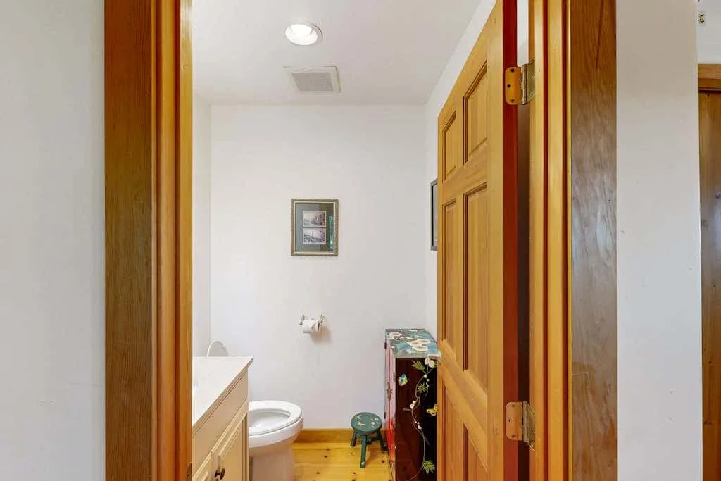 A small bathroom with a toilet, vanity, and wooden floor.