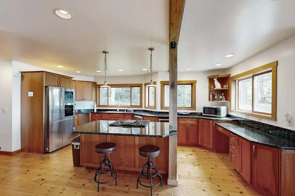 A spacious kitchen with reddish wood cabinets, dark countertops, and a central island.