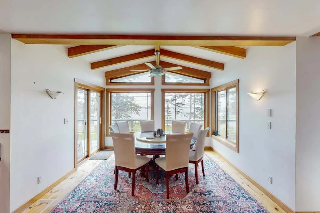A dining area with a table and chairs beneath exposed wooden ceiling beams.