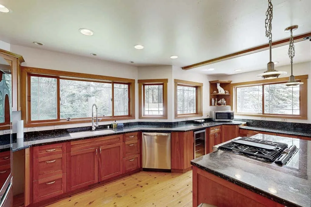 A kitchen with wooden cabinets, broad windows, and a central island.