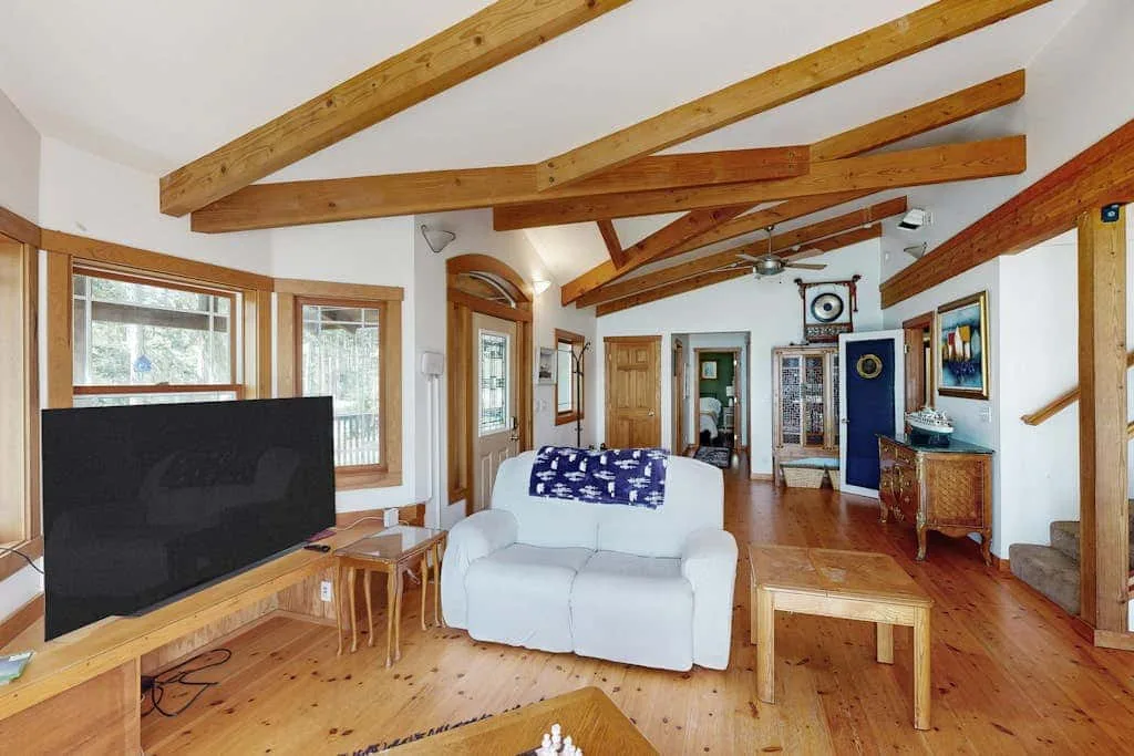 A bright living room with exposed wooden beams, seating, and a television.