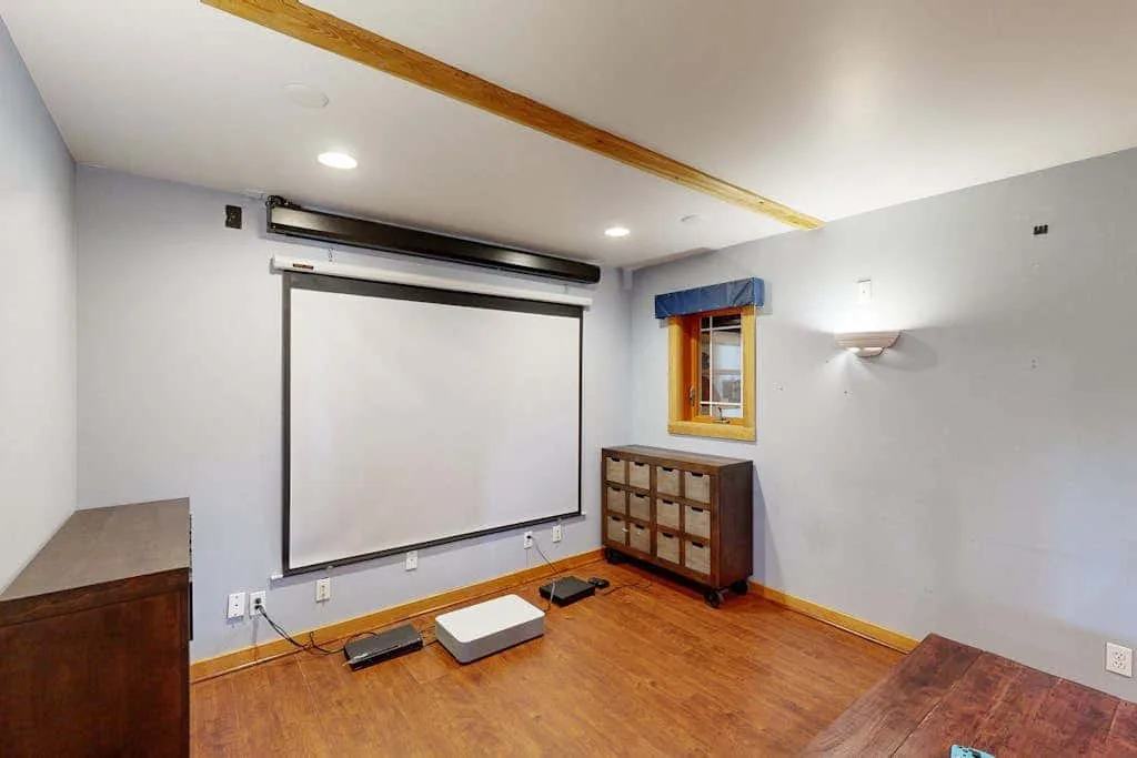 A home theater room with a large projection screen and wooden flooring.