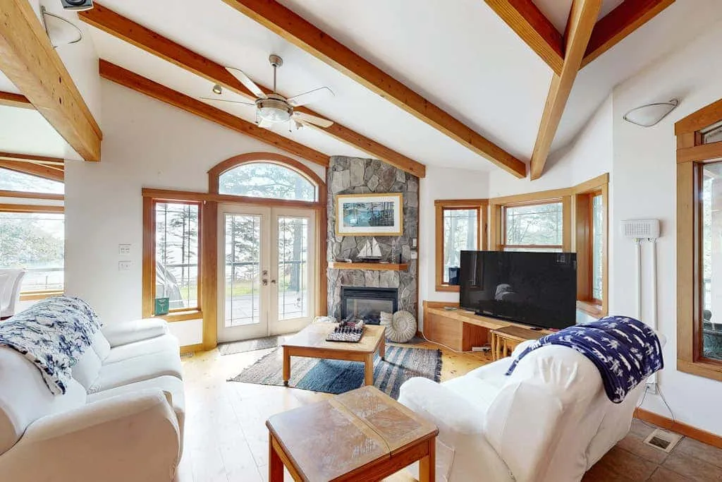 A bright living room with seating, a television, and a stone fireplace.
