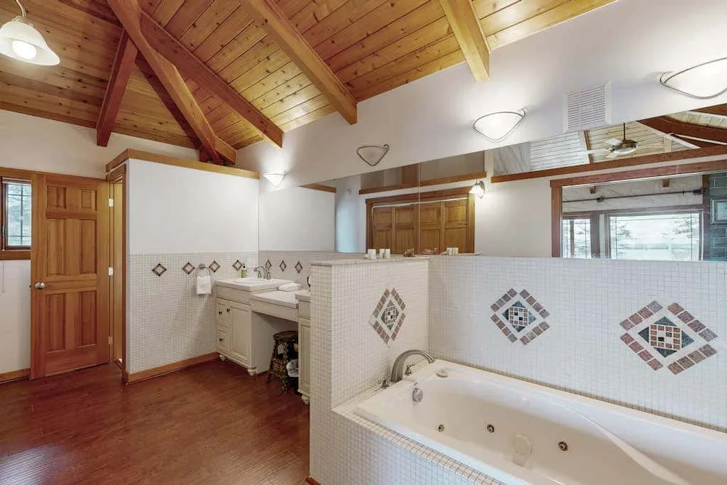 A bathroom with a tiled bathtub, sinks, and a high wooden ceiling.