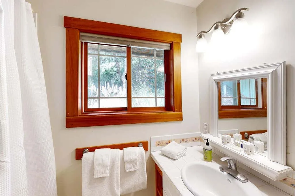 A bright bathroom vanity sits beneath a wood-framed window.