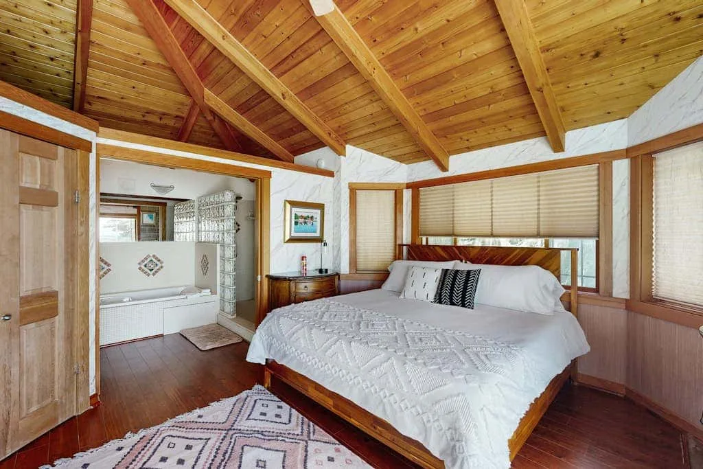 A bedroom with a bed, patterned rug, and exposed wooden ceiling beams.