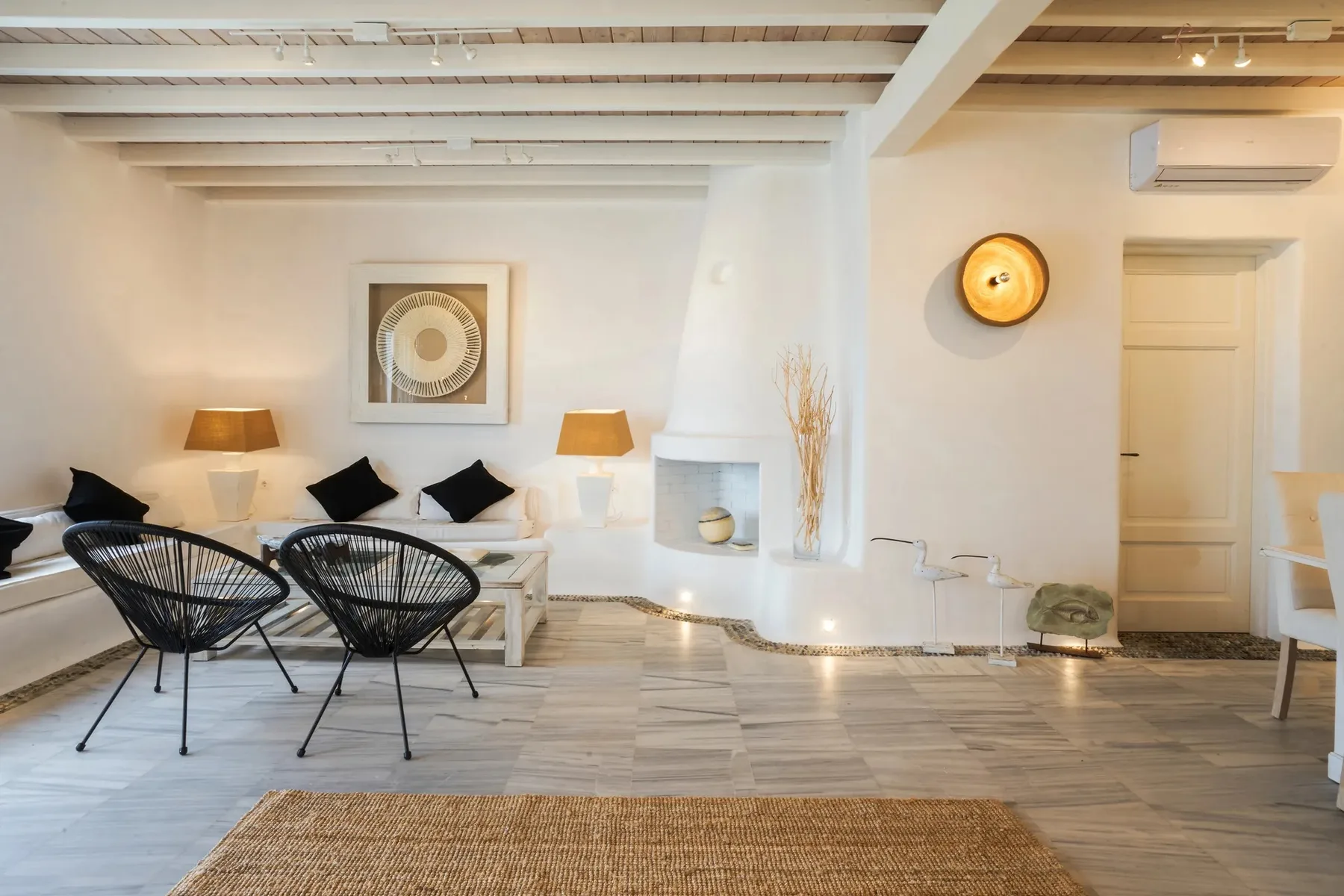 A bright living room with white seating and two dark woven chairs.