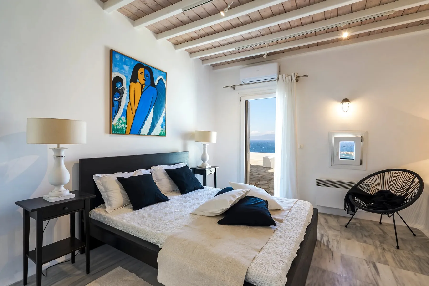 A bedroom with a bed, colorful wall art, and a doorway opening onto a sea view.