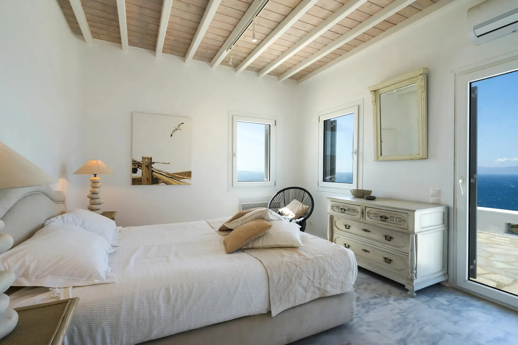 A bright bedroom with a bed, dresser, and glass doors opening to a balcony.
