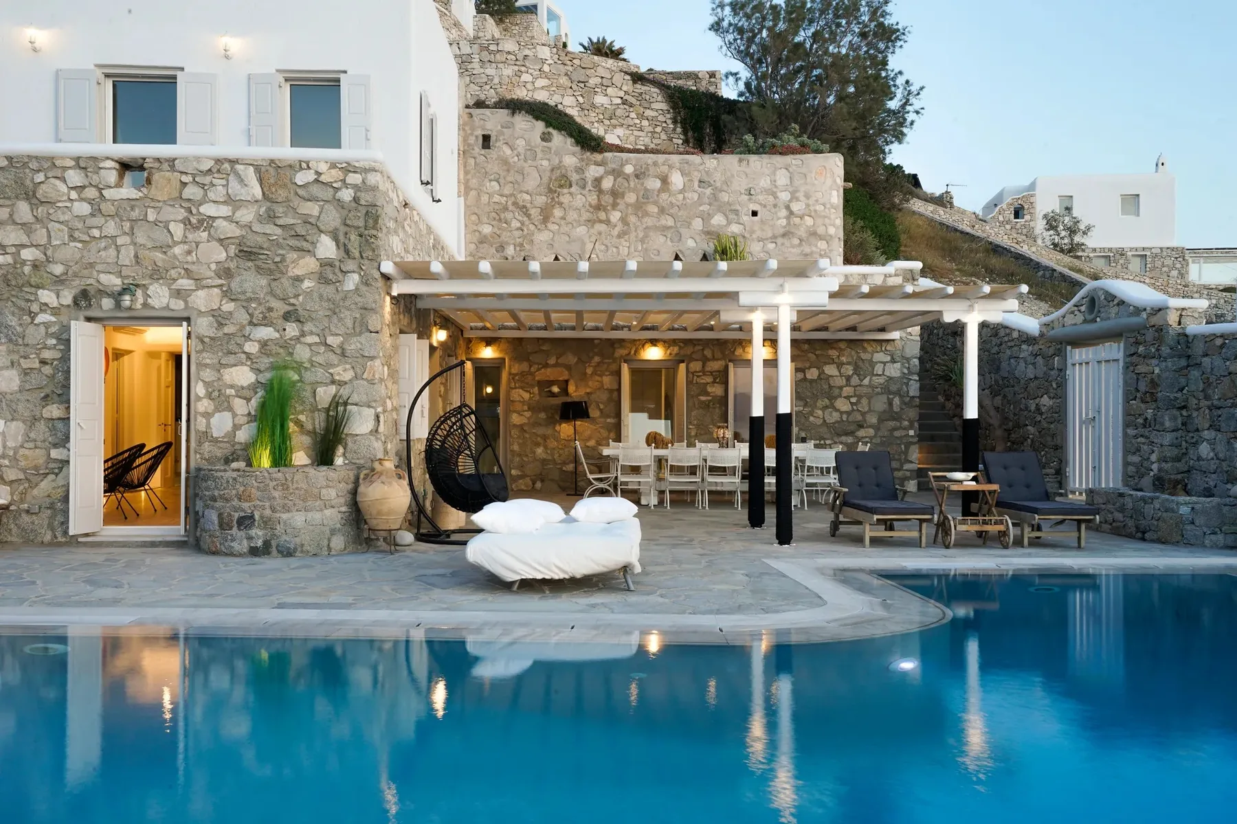 A swimming pool sits beside a stone terrace with outdoor seating.