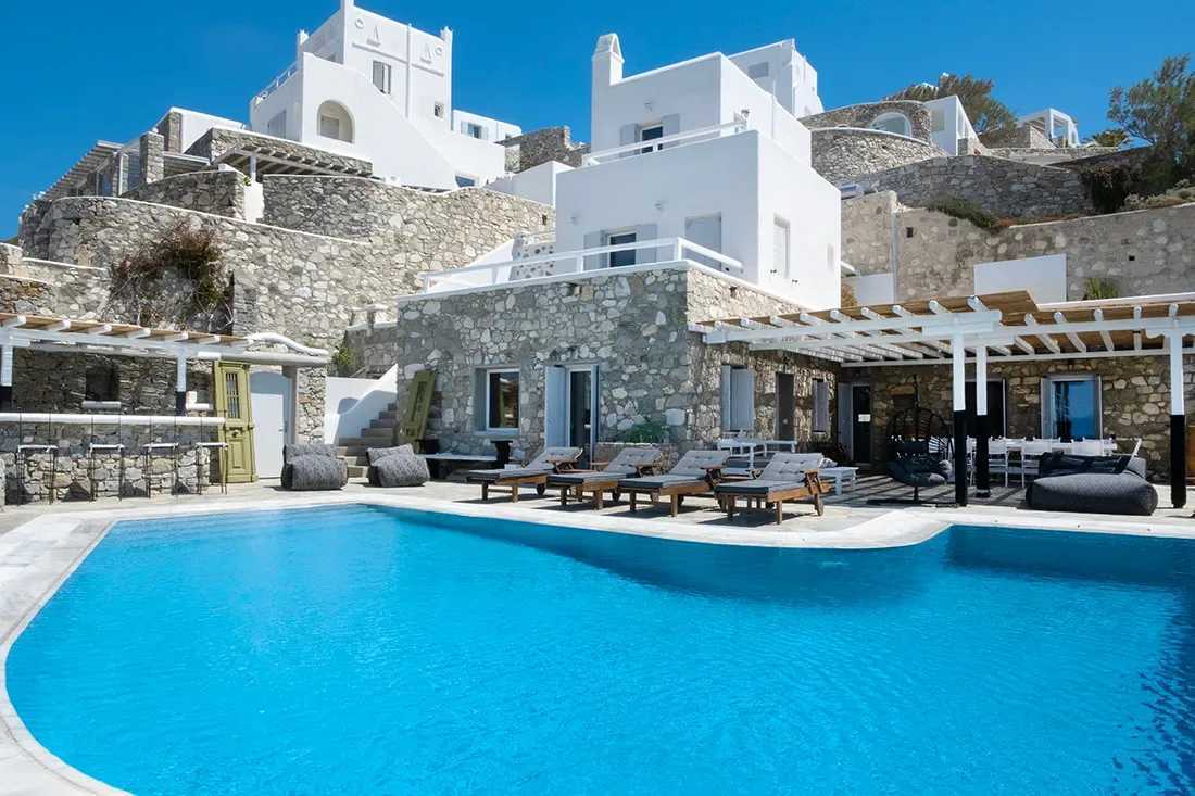 A swimming pool in front of a stone-and-white building with outdoor seating.
