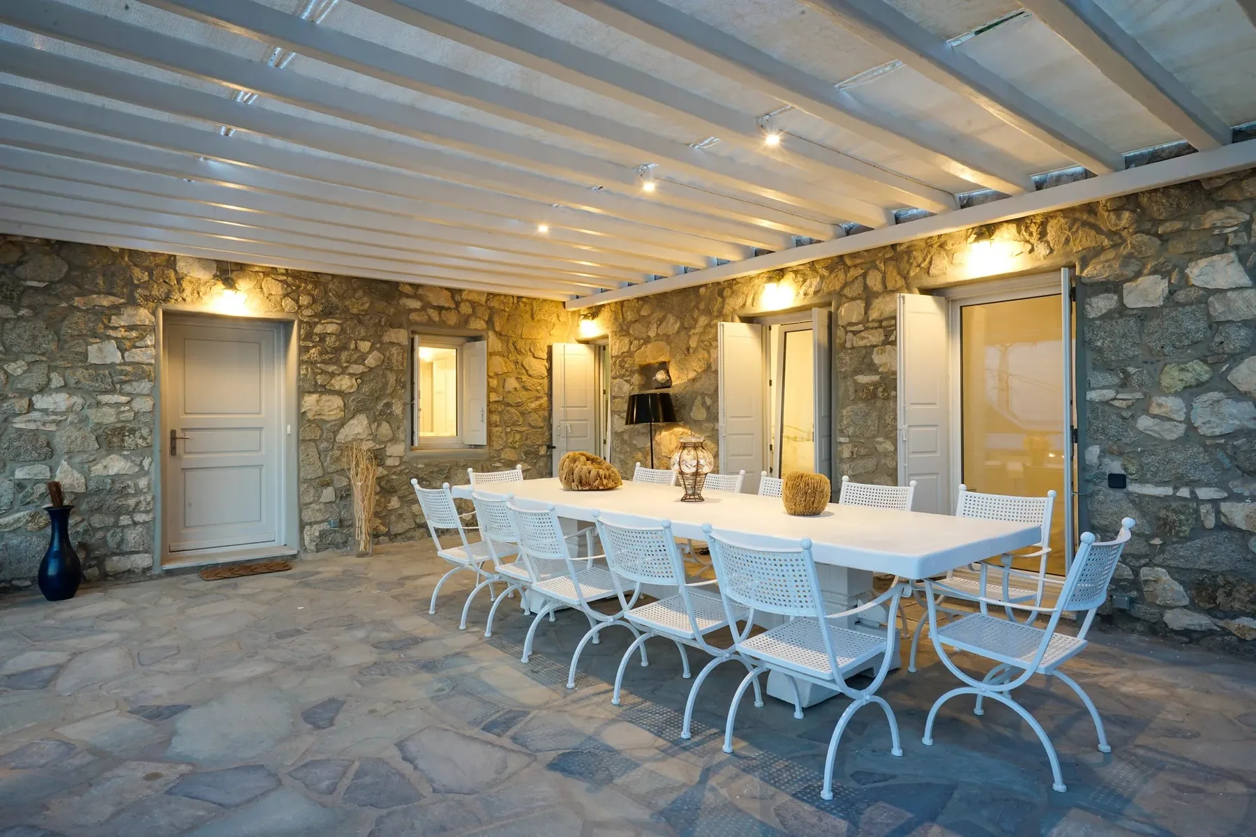 A covered dining area with a long table and white seating.
