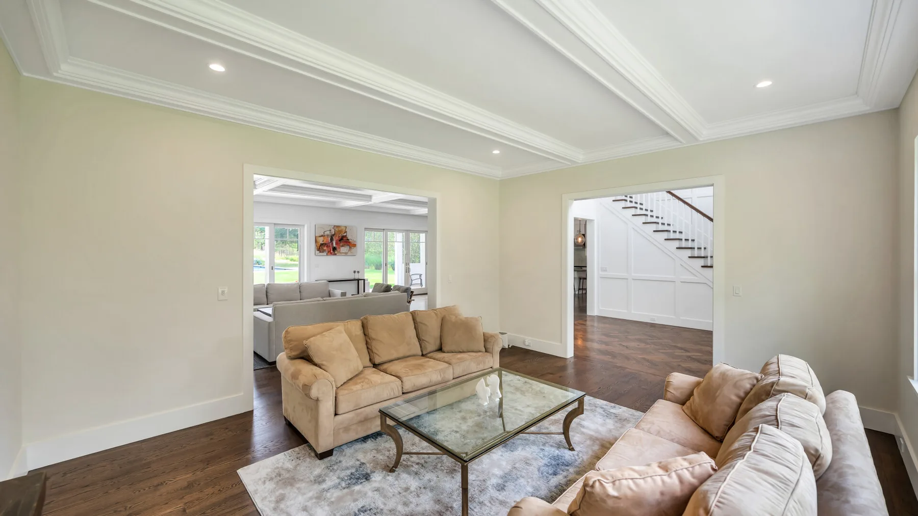 A living room with beige seating, a glass coffee table, and a staircase.