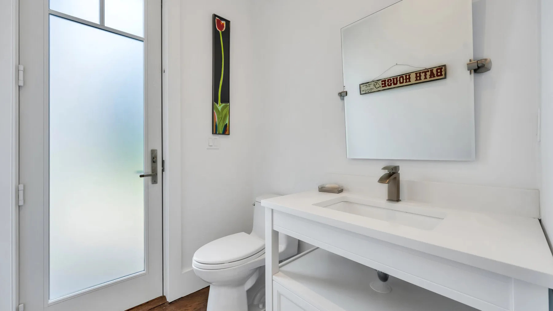A bright bathroom with a white sink, toilet, and frosted-glass door.
