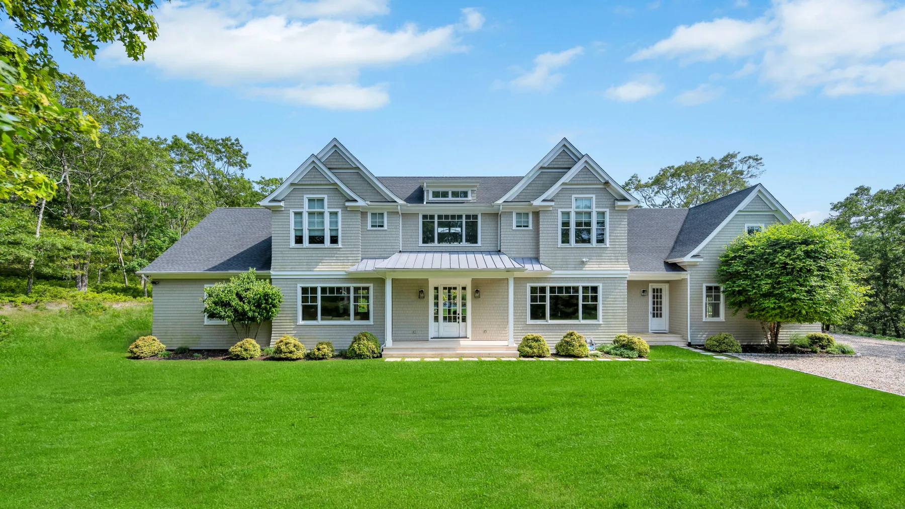 A large house stands beyond a broad green lawn, surrounded by trees.