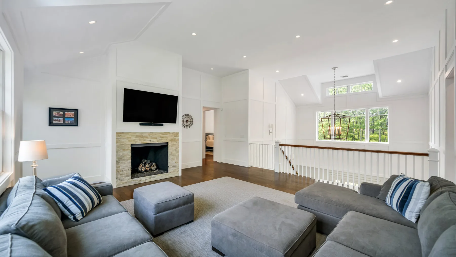 A bright living room with gray seating and a fireplace beneath a wall-mounted television.