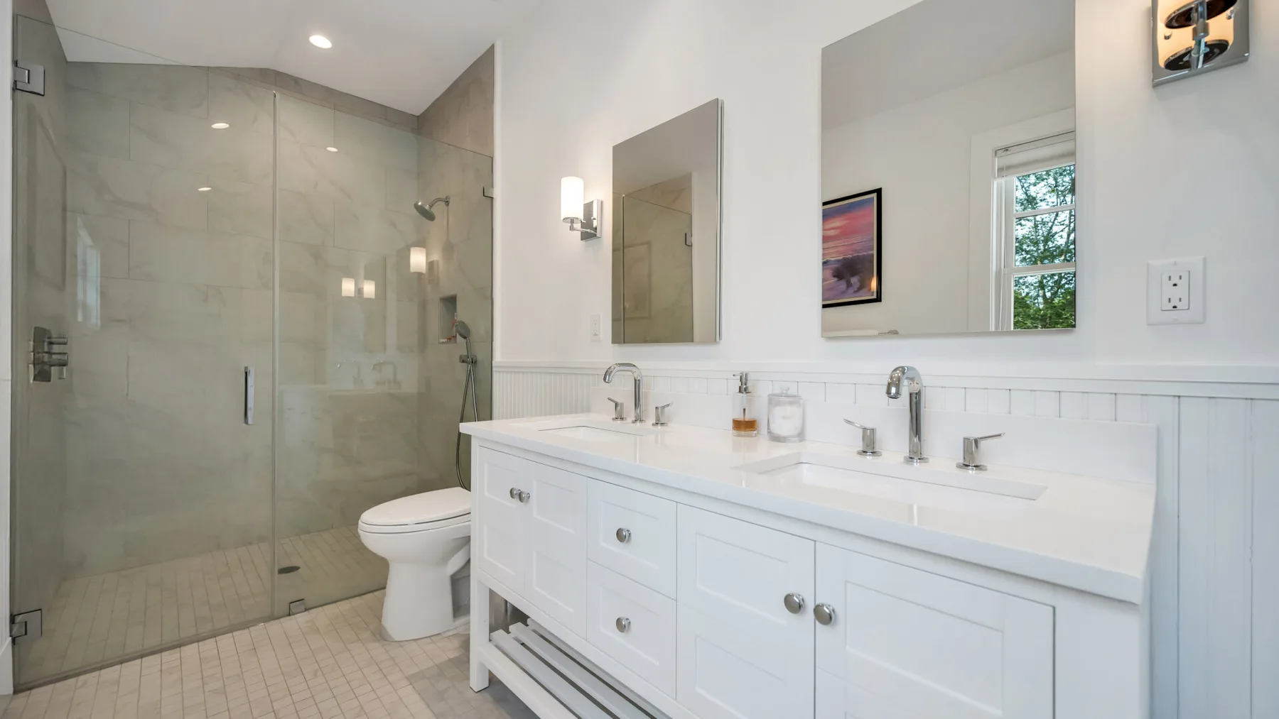 A bright bathroom with a glass shower and a long white vanity.