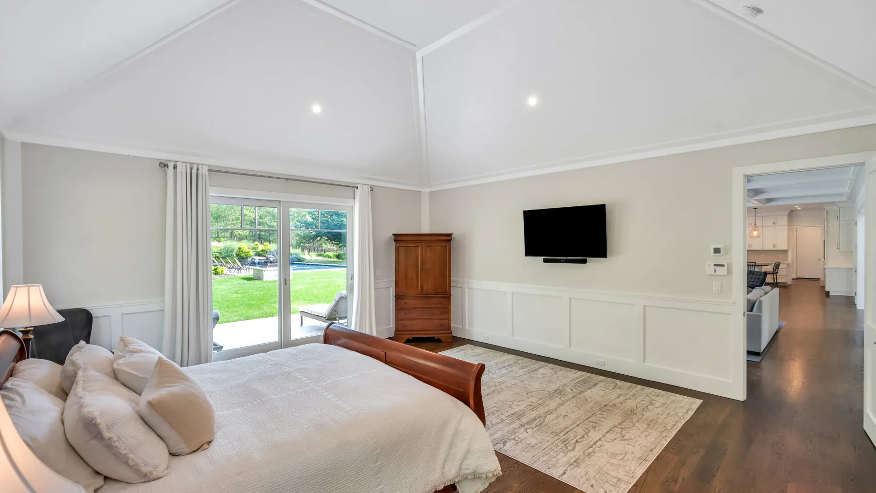 A bright bedroom with a large bed and sliding glass doors opening onto a garden.
