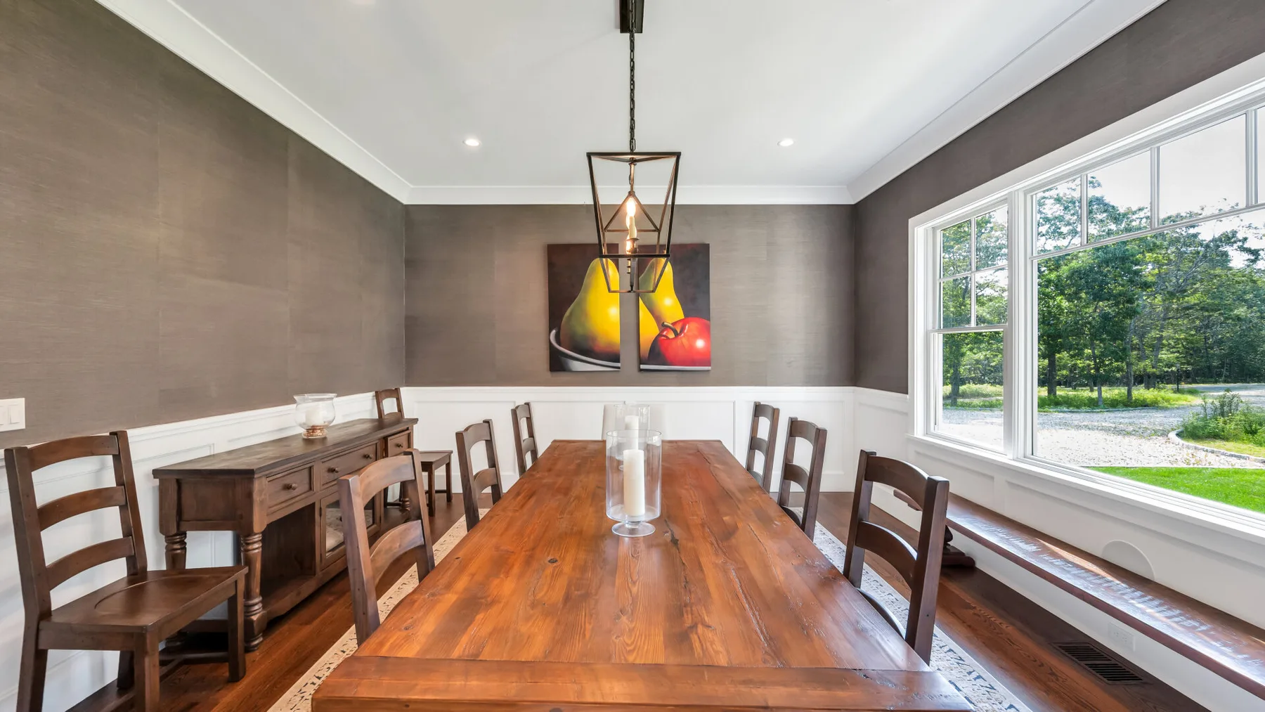 A dining room with a long wooden table, chairs, and large windows.