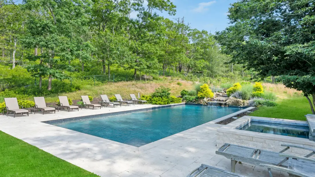Outdoor swimming pool beside a paved patio and green lawn.