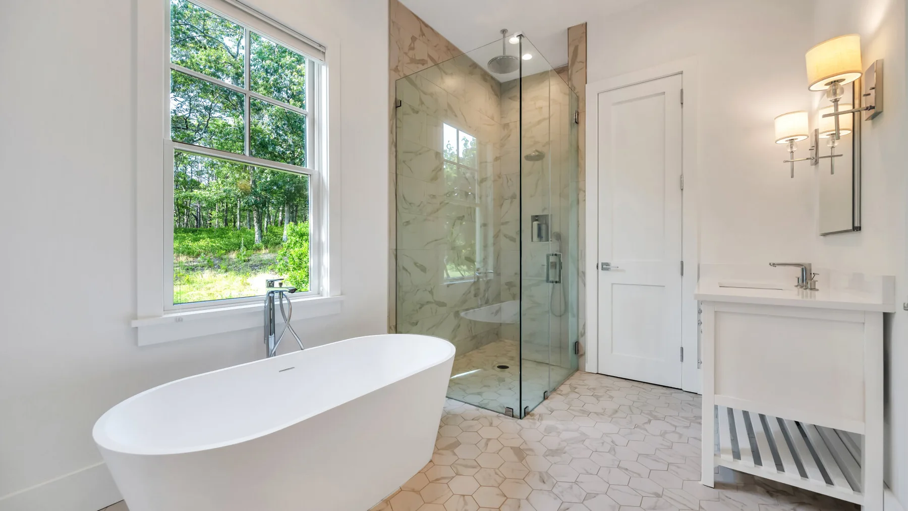 A bright bathroom features a freestanding bathtub, glass shower, and large window.
