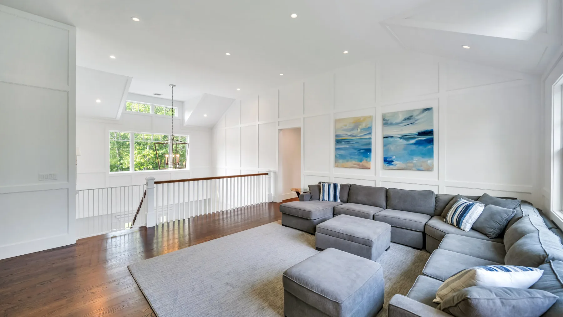 A bright living room with gray seating, a rug, and large windows.