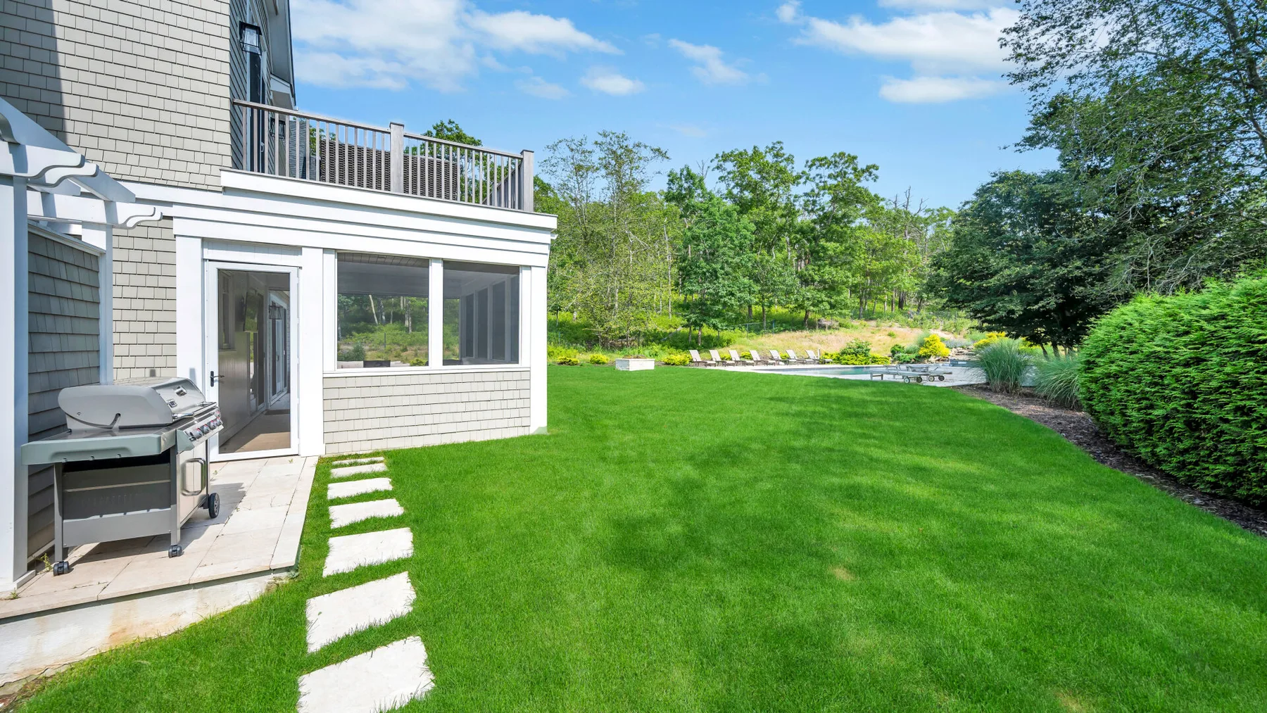 A green lawn beside a house, with a patio and trees in the background.