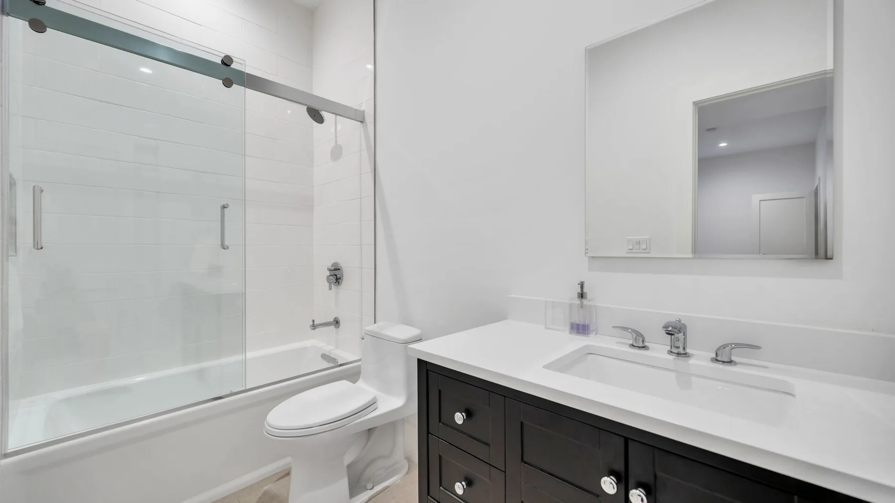 A bright bathroom with a glass shower, toilet, and wide vanity.