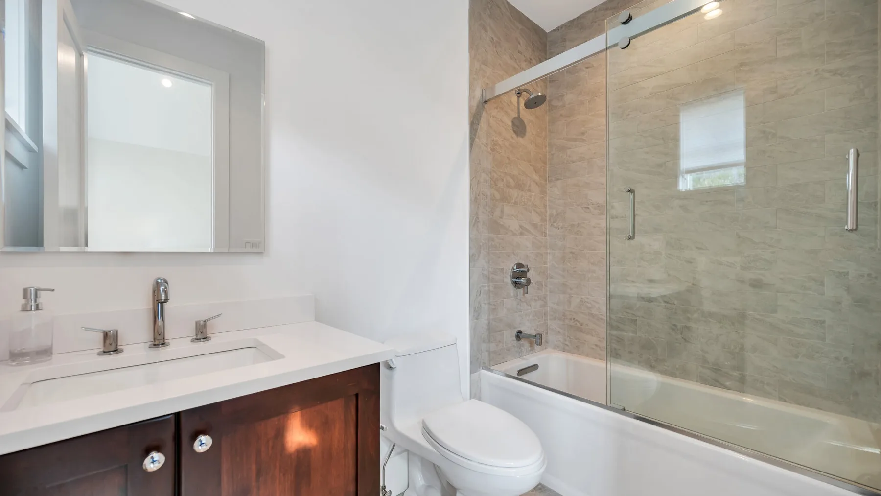 A bathroom with a vanity, toilet, and bathtub with a glass shower screen.