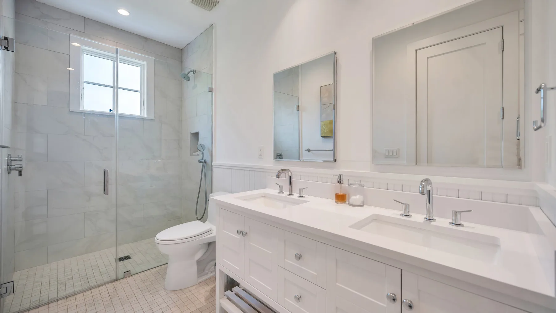 A bright bathroom with a glass shower, toilet, and long vanity.