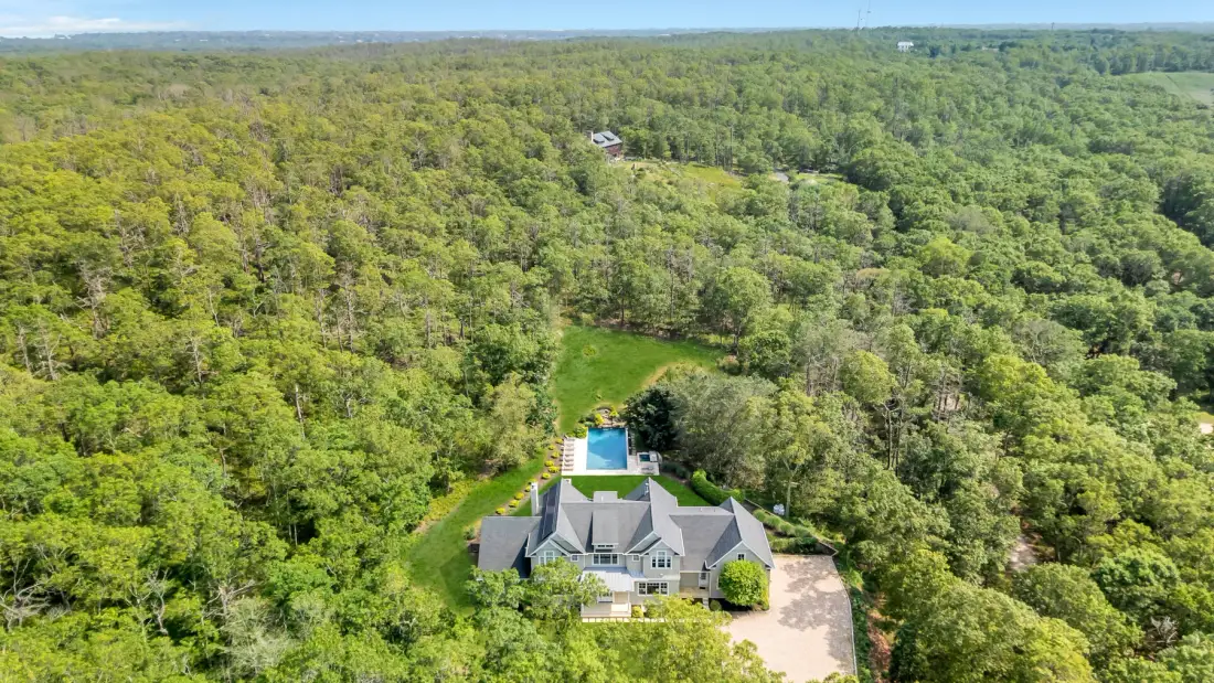 An aerial view shows a house surrounded by dense green woodland.